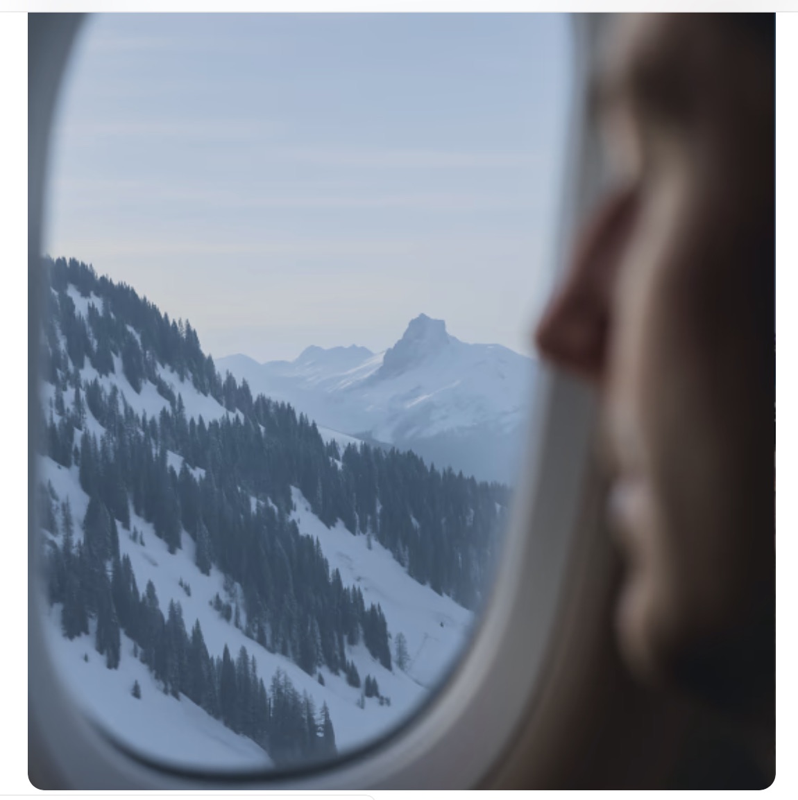 Passenger looking out a cabin window at snow-covered mountains