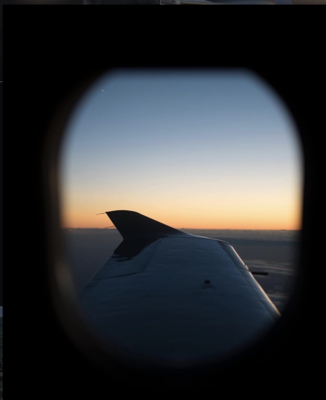 View of an aircraft wing through a cabin window at sunset